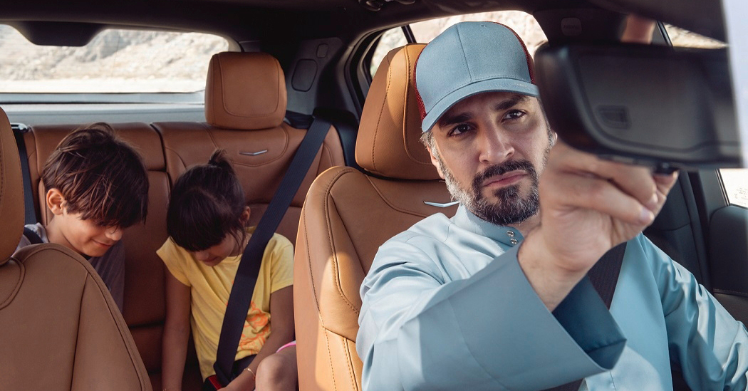 un hombre mira por el retrovisor a los niños que se abrochan el cinturón en el asiento trasero